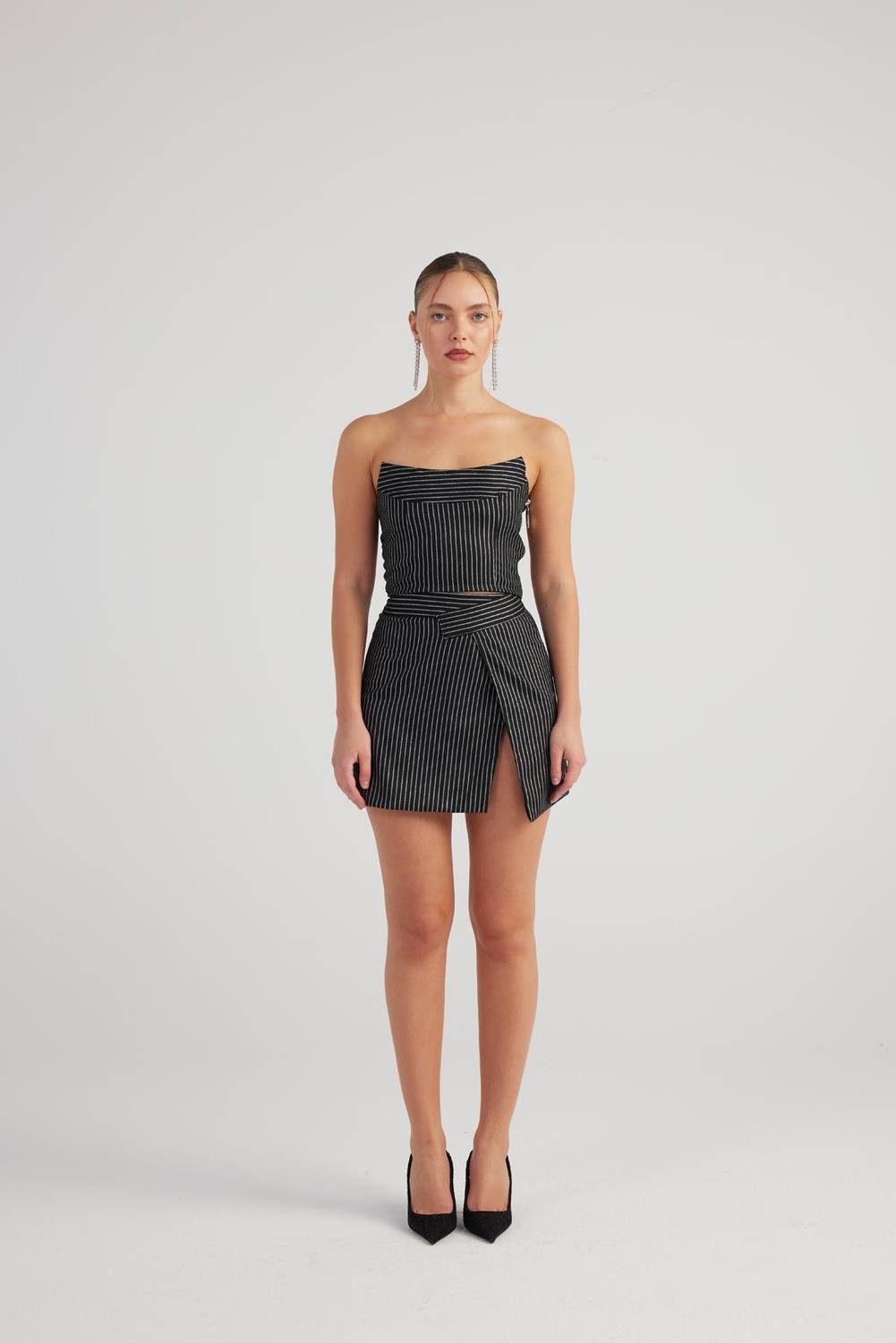 Міні-спідниця з асиметричним поясом та розрізом, модель XS, чорного кольору, з блискучими смужками